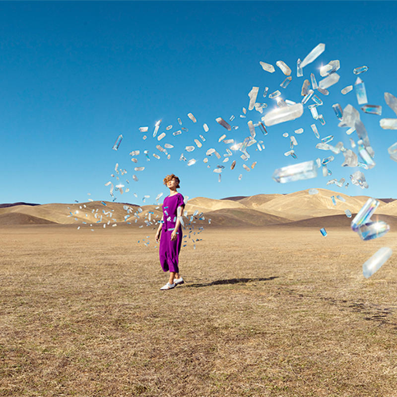 Image of a woman on a desert with crystals flying at her